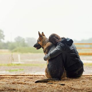 Femme assise parterre qui fait un câlin à son chien
